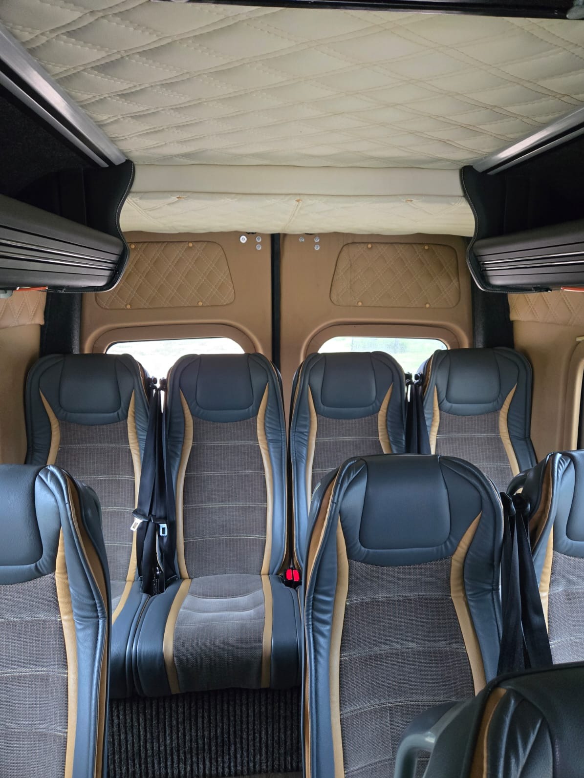 Wnętrze luksusowego busa: skórzane fotele w odcieniach szarości i beżu, pikowana podsufitka. Widok z przodu kabiny pasażerskiej na puste miejsca.