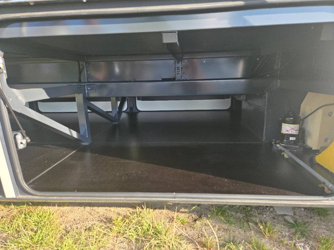 Otwarty luk bagażowy autobusu turystycznego z widoczną konstrukcją wsporczą, hydraulicznym podnośnikiem i podłogą z ciemnego tworzywa.