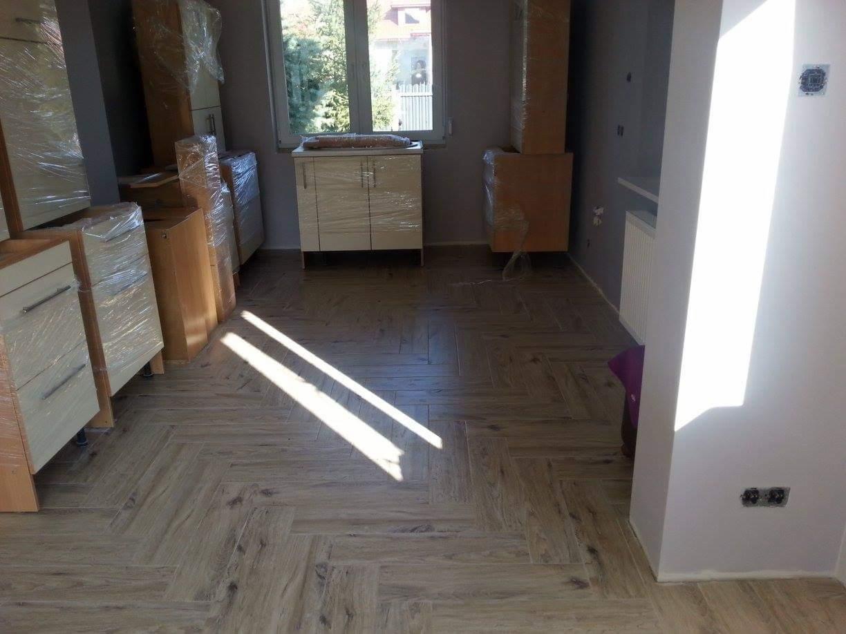 Nowe meble kuchenne w folii ochronnej, czekające na montaż w mieszkaniu w Łodzi. Widoczna podłoga z parkietu ułożonego w jodełkę.