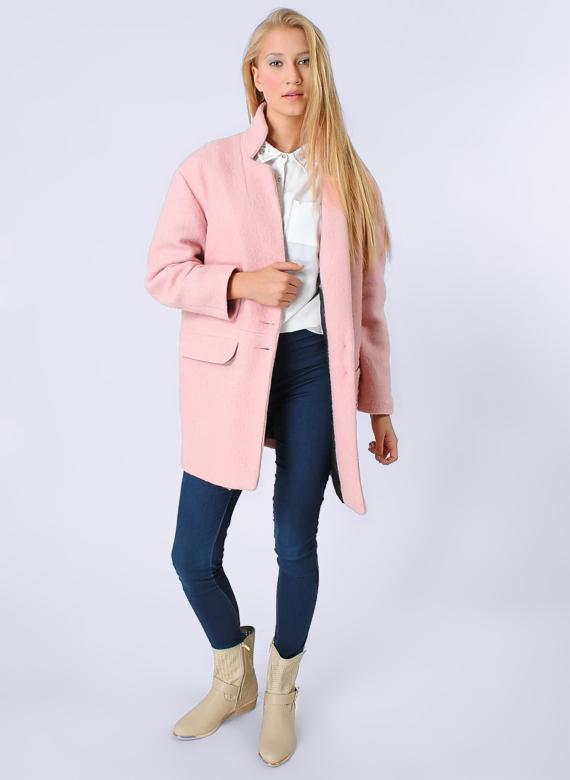 Młoda kobieta prezentuje różowy, wełniany płaszcz o prostym kroju, noszony z białą koszulą, ciemnymi jeansami i beżowymi botkami na jasnym, jednolitym tle.