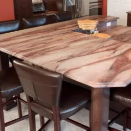 Rozległy blat z kamienia o unikalnym wzorze w kuchni w Ostrołęce, otoczony eleganckimi, brązowymi krzesłami barowymi. Ciepłe oświetlenie podkreśla detale.