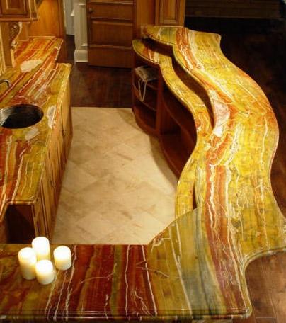 Unikalny blat kamienny z onyksu w kuchni, o nieregularnym kształcie i bogatym, wielobarwnym wzorze. Widoczne trzy świece i fragment podłogi.