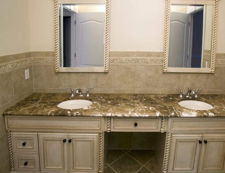 Łazienka z dwoma umywalkami na marmurowym blacie i kremowymi szafkami. Nad nimi lustra w zdobionych ramach i dekoracyjne płytki ścienne.