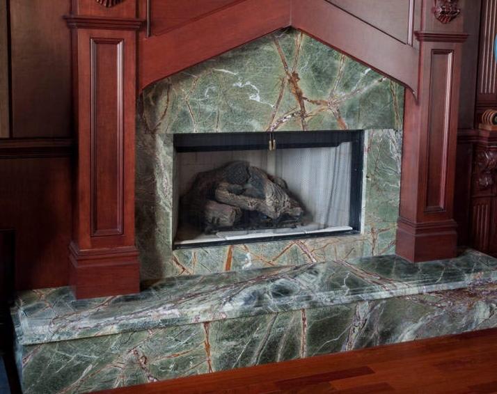 Marmurowy kominek z drewnianą obudową i imitacją ognia. Zielony kamień z wyraźnym wzorem żyłkowania. Klasyczny design z ozdobnymi detalami.