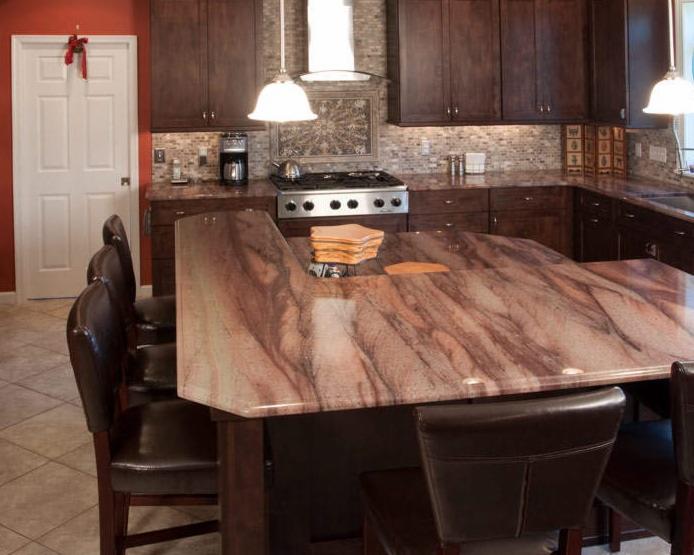 Kuchenna wyspa z blatem z kamienia o unikalnym wzorze, brązowe szafki, oświetlenie punktowe, dekoracyjna mozaika nad kuchenką. Widok z bliska na blat.