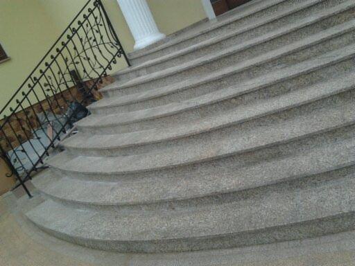Granitowe schody wewnętrzne z czarną, metalową balustradą o dekoracyjnym wzorze liści. Widoczny fragment kolumny. Ujęcie z dołu, podkreślające zakrzywiony kształt.