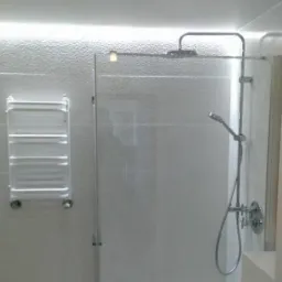 Nowoczesna łazienka: szklana kabina prysznicowa z deszczownicą i słuchawką, grzejnik drabinkowy na teksturowanej ścianie, oświetlenie LED podsufitowe.