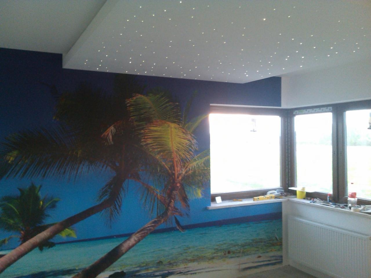 Pokój z fototapetą przedstawiającą plażę z palmami i sufitem podwieszanym z oświetleniem punktowym imitującym gwiazdy.