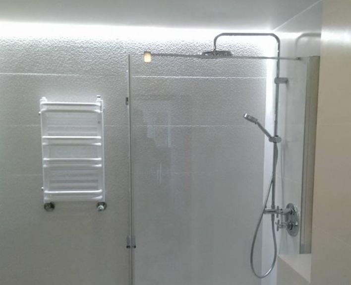 Nowoczesna łazienka: szklana kabina prysznicowa z deszczownicą i słuchawką, grzejnik drabinkowy na teksturowanej ścianie, oświetlenie LED podsufitowe.