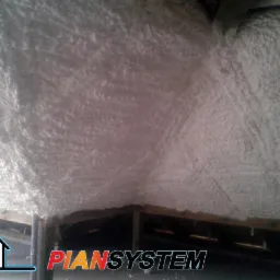 Izolacja poddasza pianą natryskową, widok z dołu. Aplikacja piany widoczna na skośnych powierzchniach dachu i stropie. Widoczne elementy konstrukcyjne.