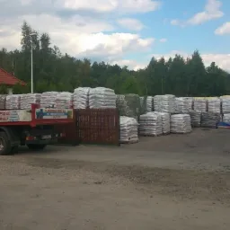 Składowisko workowanego opału z widocznym czerwonym autem dostawczym z dźwigiem na tle domu z czerwoną dachówką