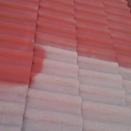 Częściowo pomalowany dach z czerwonej dachówki cementowej, widoczna granica pomiędzy pomalowaną i niepomalowaną powierzchnią, obok rynna.