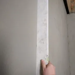 Sprawdzanie pionu ściany po nałożeniu tynku w Nowogrodźcu za pomocą poziomicy, widoczne ślady po ołówku.