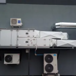 Zewnętrzna instalacja wentylacyjna z centralą, kanałami wentylacyjnymi i jednostkami klimatyzacyjnymi zamontowana na szarej ścianie budynku. Widoczne marki Haier i Midea.