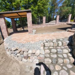 Garden Mission Possible Twój ogród to nasza misja - Zewnętrzny taras z nieregularnych, beżowo-czerwonych płyt, otoczony kamiennym murkiem i schodami z otoczaków. Obok przygotowany teren pod zieleń.
