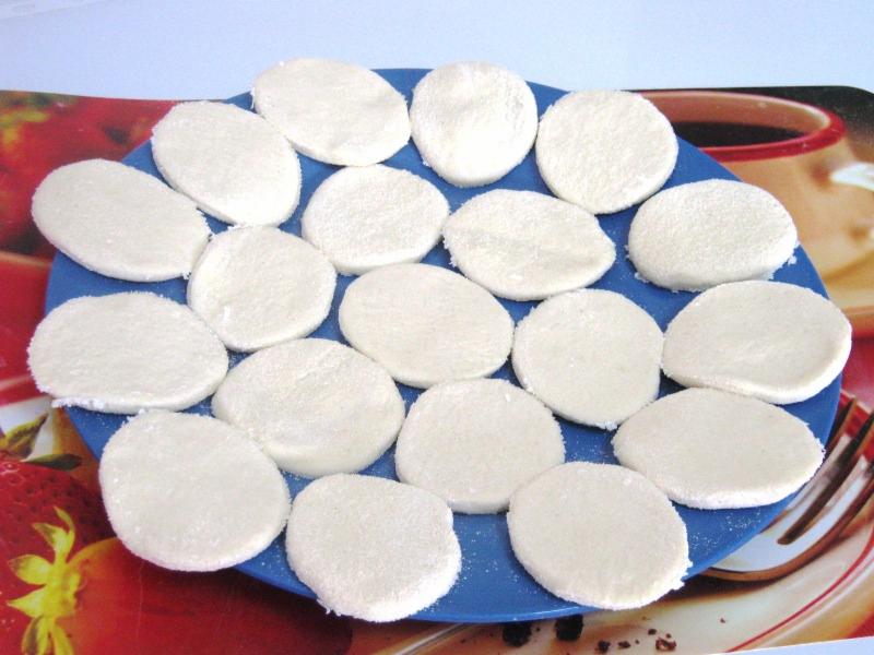 Surowe krążki ciasta na pierogi ułożone na niebieskim talerzu, na tle podkładki z motywem truskawek i filiżanki kawy.