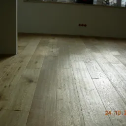 Wycyklinowana, drewniana podłoga w odcieniach beżu i brązu, z widoczną datą 24.10.2009 w prawym dolnym rogu, prezentująca efekt renowacji.
