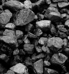 Góra brył antracytu o nieregularnych kształtach i matowej powierzchni, ułożonych jedne na drugich, z widoczną strukturą węgla.