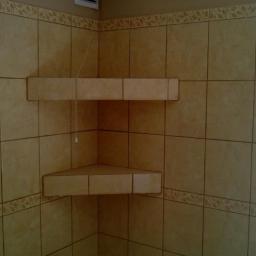 Bart-Bud - Beżowe płytki z dekoracyjnym pasem i półkami narożnymi w łazience. Widoczny fragment okna po prawej stronie kadru.