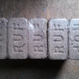 Pięć sprasowanych kostek brykietu RUF, owiniętych folią, leżących na drewnianej powierzchni. Kostki mają wytłoczone litery RUF.