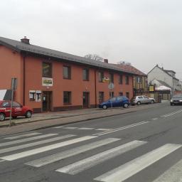 Salon Firmowy DAKO - Budynek firmy Uni Blach z ekspozycją blach dachowych i zaparkowanym czerwonym autem reklamowym. Widok na ulicę z przejściem dla pieszych.