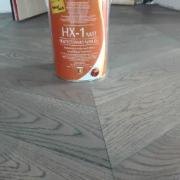 Wosk olejny HX-1 Mat firmy HartzLack na tle ułożonej podłogi z paneli w jodełkę, widoczne naturalne usłojenie drewna.
