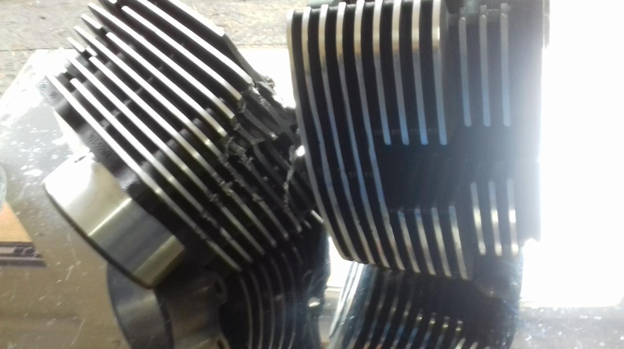 Uszkodzony, żebrowany blok silnika motocyklowego z widocznymi pęknięciami i śladami naprawy, sfotografowany w warsztacie.