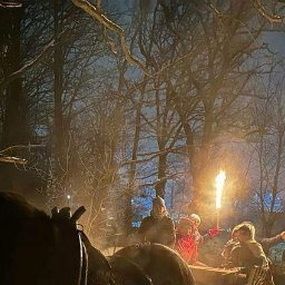 Spec-Group - Nocny przejazd bryczką przez ośnieżony las, grupa osób trzymająca płonące pochodnie, widok na zaprzęg konny w ciemności.