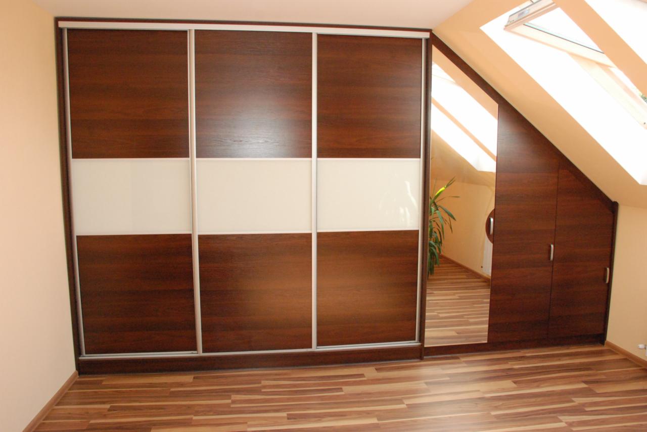 Szafa wnękowa z przesuwnymi drzwiami w odcieniach brązu i bieli, z lustrem na jednym skrzydle, dopasowana do skosu poddasza. Widoczny drewniany parkiet.