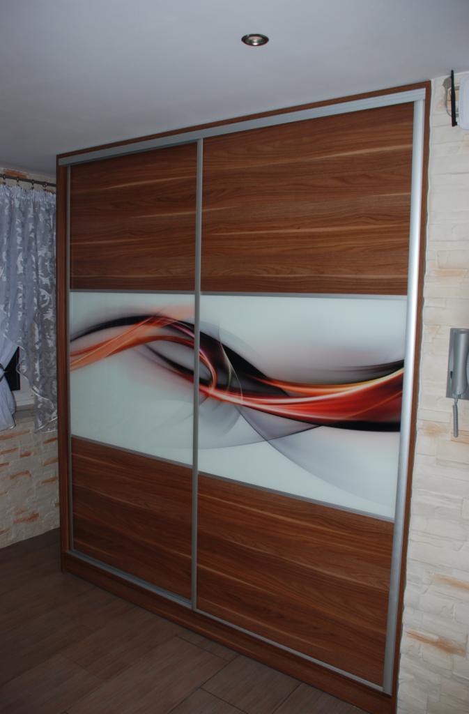 Drewniana szafa przesuwna z abstrakcyjnym wzorem w odcieniach czerwieni i szarości na szklanych frontach, srebrne obramowanie, widok z perspektywy podłogi.