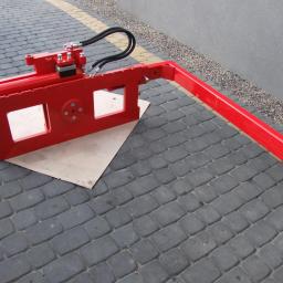 Jg Serwis-Truck - Czerwony osprzęt do wózka widłowego z hydraulicznymi przewodami, leżący na kostce brukowej. Widok z boku, z bliska.