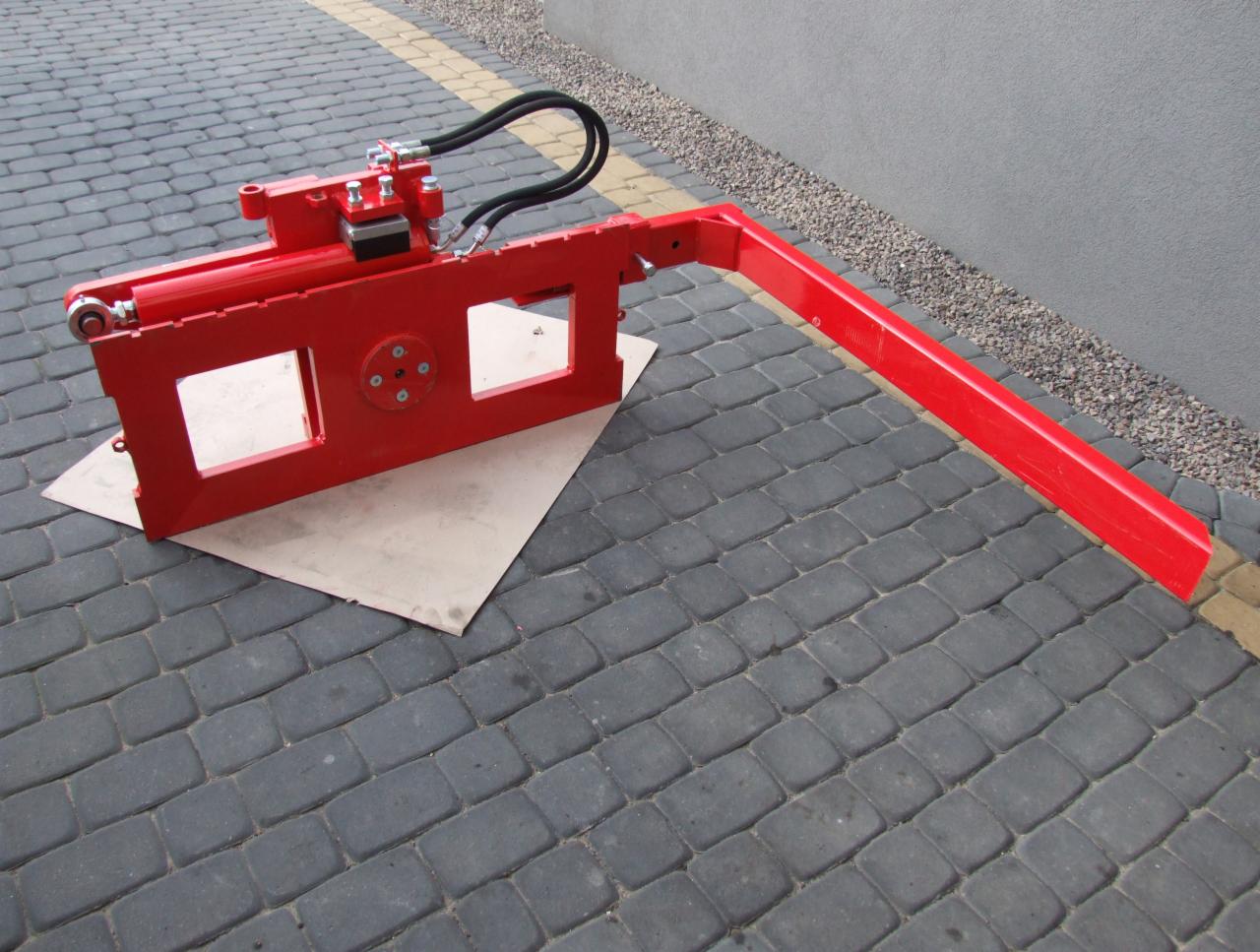 Czerwony osprzęt do wózka widłowego z hydraulicznymi przewodami, leżący na kostce brukowej. Widok z boku, z bliska.