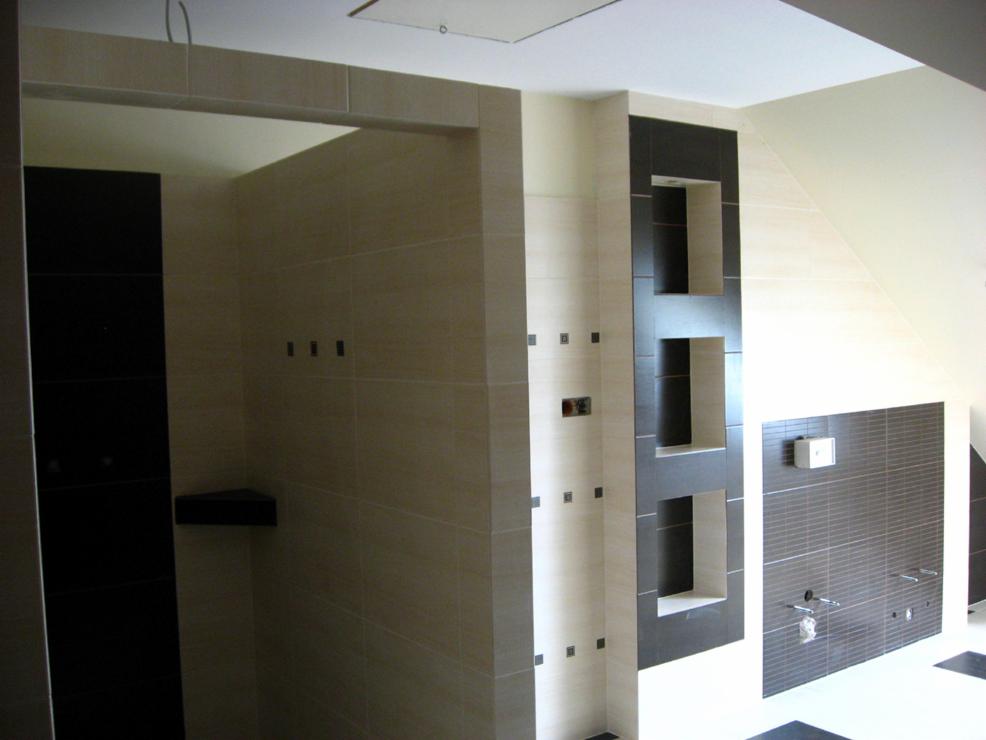 Wykończona łazienka z beżowymi i ciemnobrązowymi płytkami. Wnęki w ścianie, armatura zamontowana. Nietypowe wykończenie poddasza.