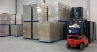 Magazyn z paletami środków czystości transportowanych wózkiem widłowym. Pakunki owinięte folią, widoczny operator wózka.