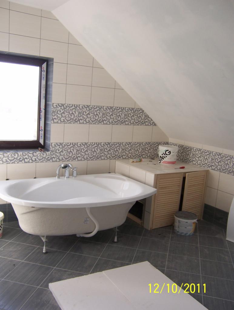 Biała wanna na nóżkach w łazience na poddaszu, dekoracyjne płytki z motywem roślinnym, widoczna data na podłodze: 12/10/2011.