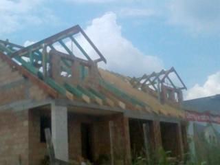 Budowa domu w trakcie wznoszenia konstrukcji drewnianej dachu, widoczne elementy więźby dachowej, pustaki ceramiczne i fragment niebieskiego nieba z chmurami.