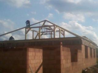 Montaż drewnianej konstrukcji dachu na budynku w trakcie budowy w Nowogrodźcu, widoczni dwaj pracownicy na wysokościach.