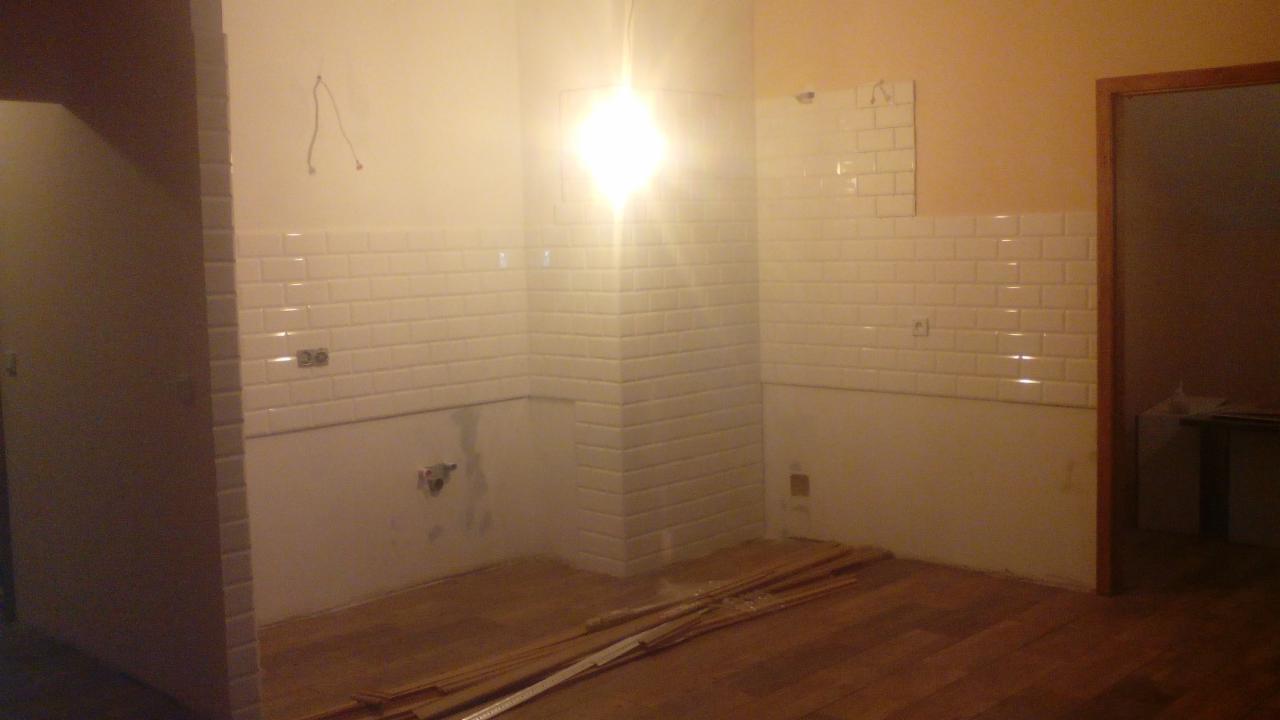 Wnętrze w trakcie remontu: częściowo wyłożone białe, błyszczące płytki typu metro na ścianach, surowe podłoże podłogi, widoczne kable i niedokończone fragmenty.