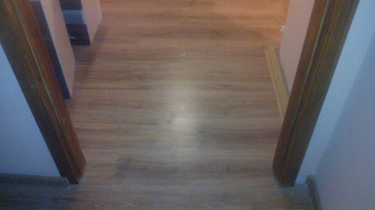 Ułożona podłoga z paneli drewnopodobnych w przejściu między pomieszczeniami, widoczne ościeżnice drzwiowe, ujęcie z góry.