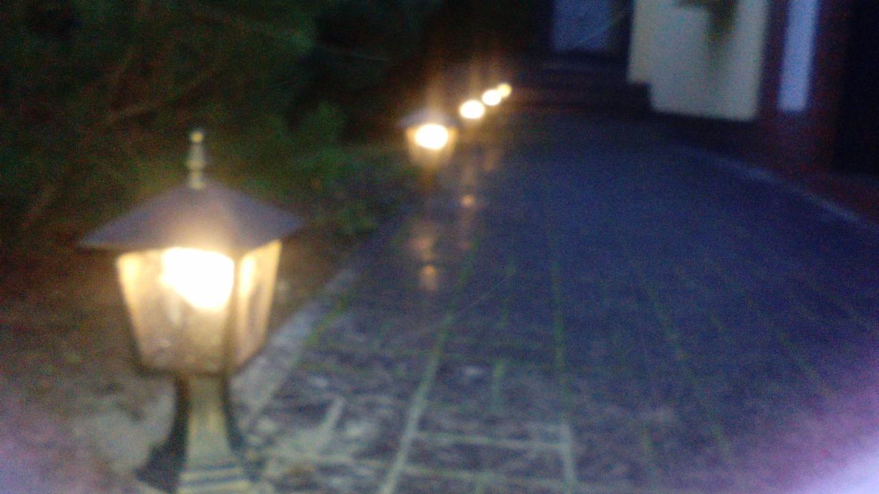 Oświetlona ścieżka z kostki brukowej prowadząca do domu, oświetlona przez szereg lamp ogrodowych w nocnej scenerii.