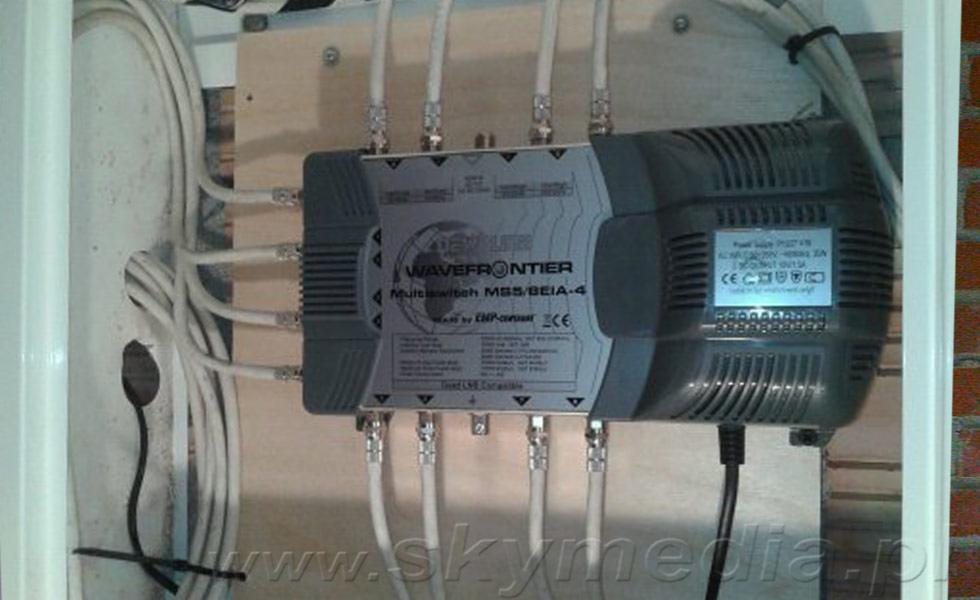 Rozdzielacz antenowy Wavefrontier MSS/BEIA-4 z podłączonymi kablami, zamontowany na drewnianej płycie wewnątrz pomieszczenia, widoczne przewody i zasilanie.