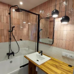 Nowoczesna łazienka z różowymi, pionowo ułożonymi płytkami, czarną armaturą, szklanym panelem prysznicowym, drewnianym blatem pod umywalką i wiszącymi lampami.