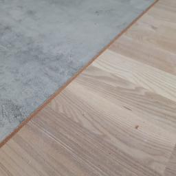 BUD-SYSTEM Marek Bojczuk - Połączenie płytek imitujących beton i jasnej drewnianej podłogi, widoczny przekrój warstw podłogi na styku materiałów.