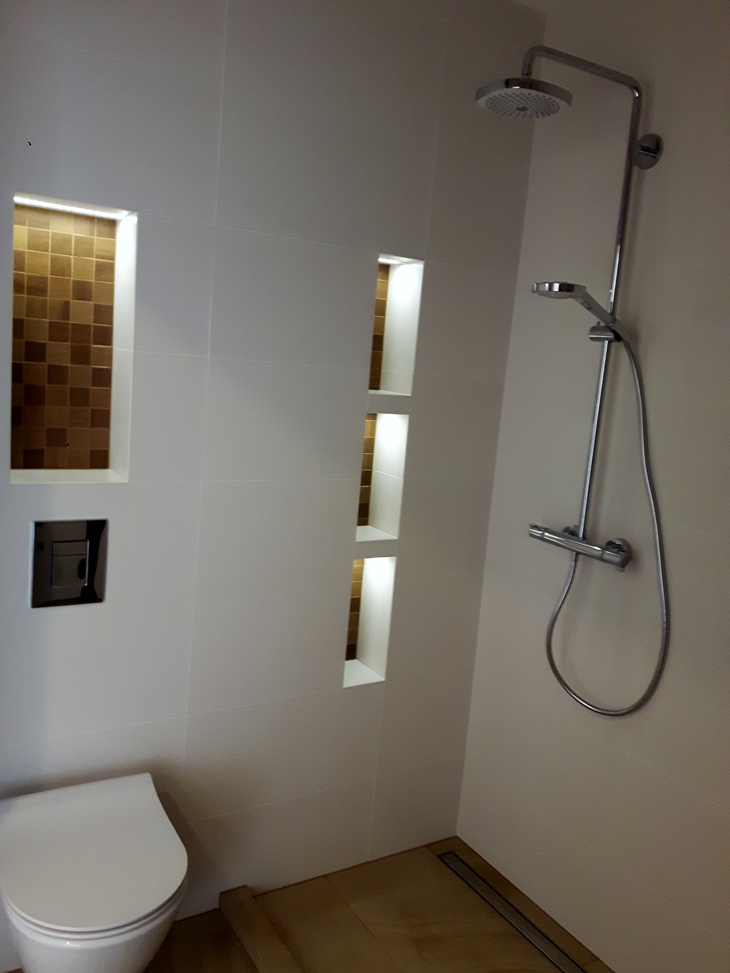 Nowoczesna łazienka z białymi płytkami, chromowaną armaturą prysznicową i wnękami z mozaiką w ścianie.