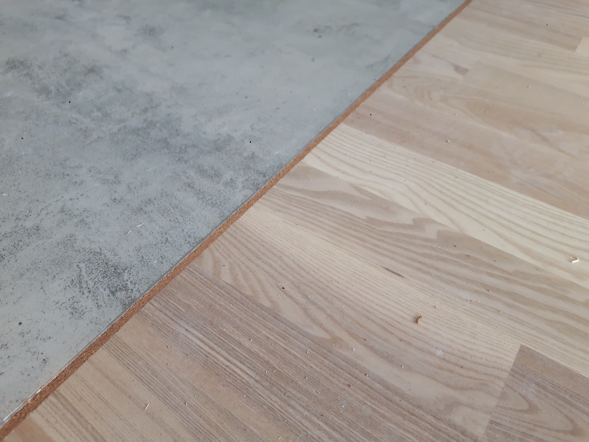 Połączenie płytek imitujących beton i jasnej drewnianej podłogi, widoczny przekrój warstw podłogi na styku materiałów.