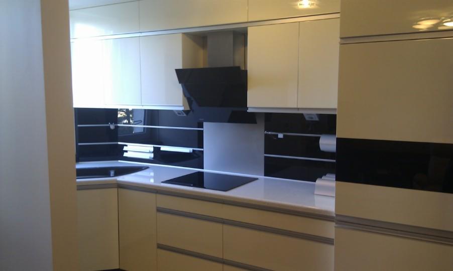 Jasna kuchnia z czarnymi akcentami: błyszczące fronty szafek, czarny panel nad blatem i nowoczesny okap. Minimalistyczny design, oświetlenie punktowe.