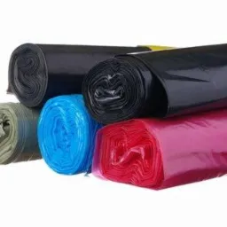 Kolorowe rolki worków na śmieci: czarne, niebieskie, czerwone i szare, ułożone w stos na białym tle. Widoczne marszczenia i połysk plastiku.