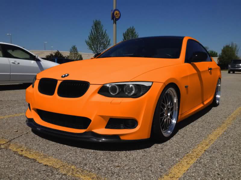 Pomarańczowe BMW E92 po zmianie koloru folią Plastidip, z czarnym dachem i karbonowym splitterem, zaparkowane na parkingu.