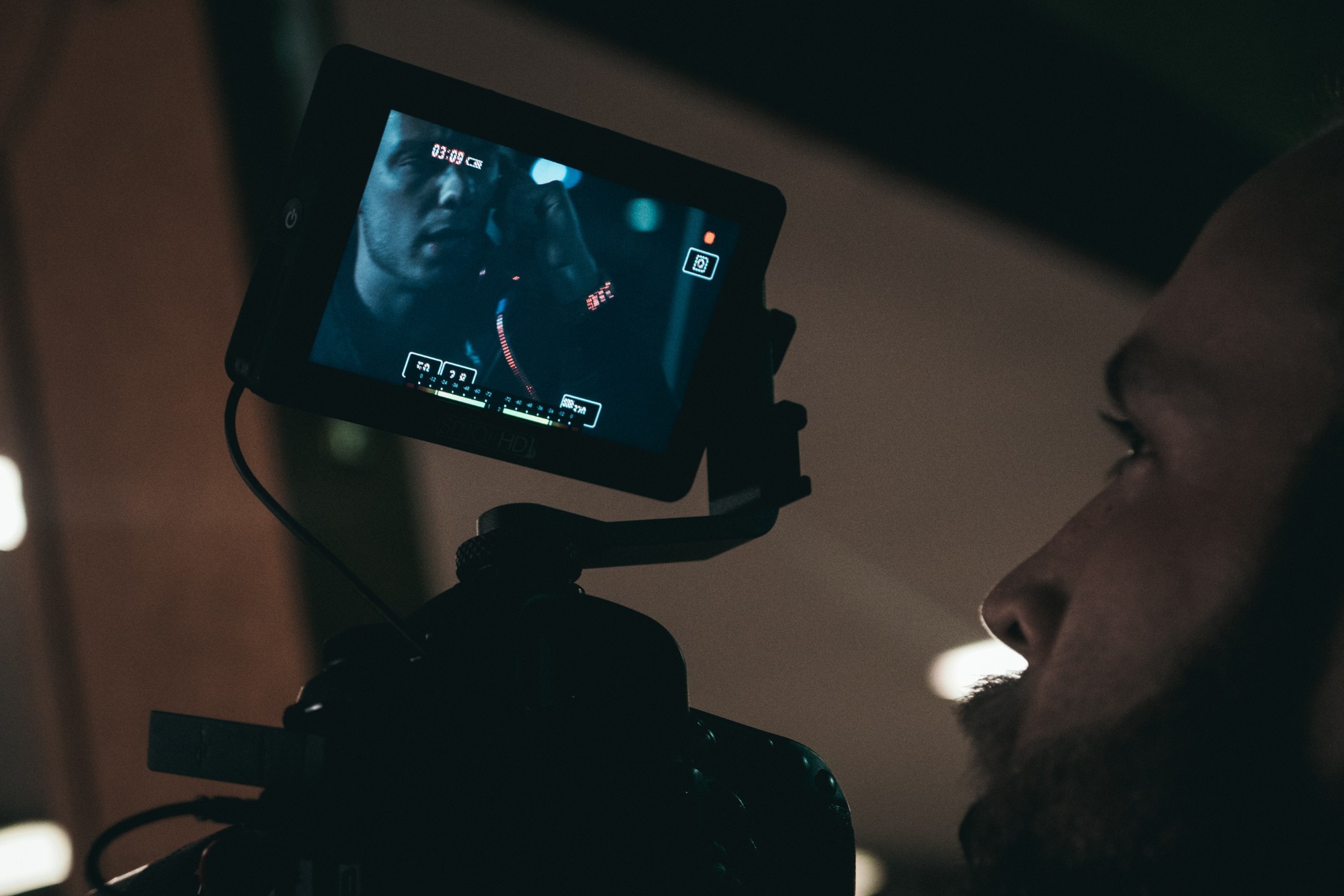Kamerzysta obserwuje nagrywany obraz na monitorze kamery, widoczny profil twarzy operatora i parametry nagrywania na ekranie.