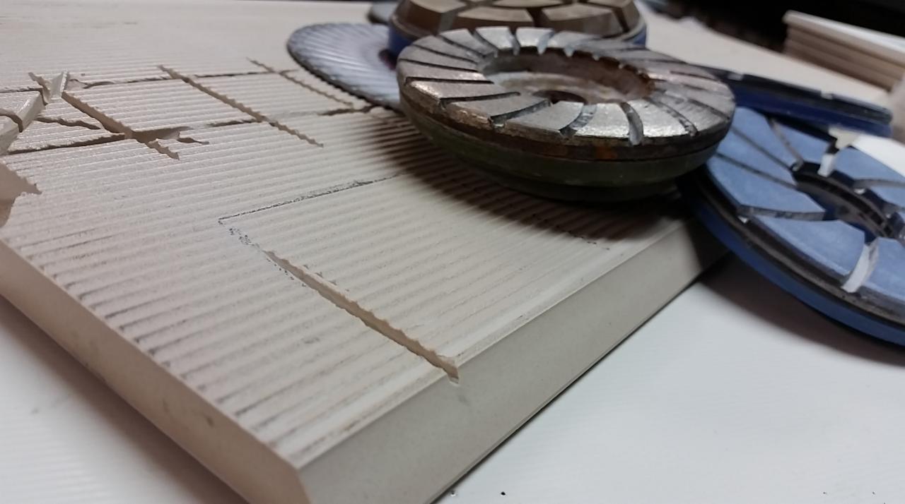 Płytka gresowa z widocznymi nacięciami i ukosowanymi krawędziami, obok tarcze diamentowe do cięcia i szlifowania płytek.